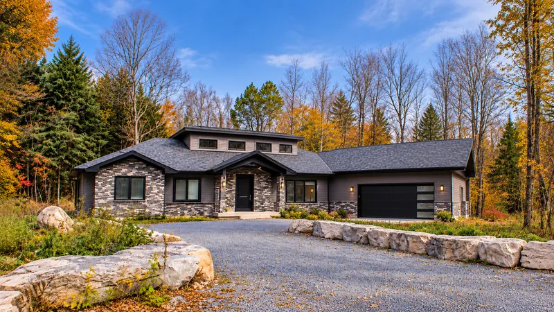 Stone-clad modern residence in an autumn woodland with a gravel driveway